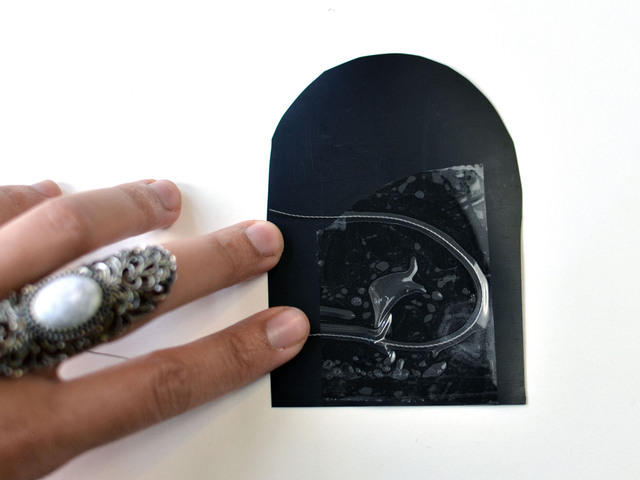 A hand holds a heel-shaped piece of black Velostat with conductive thread taped to it.